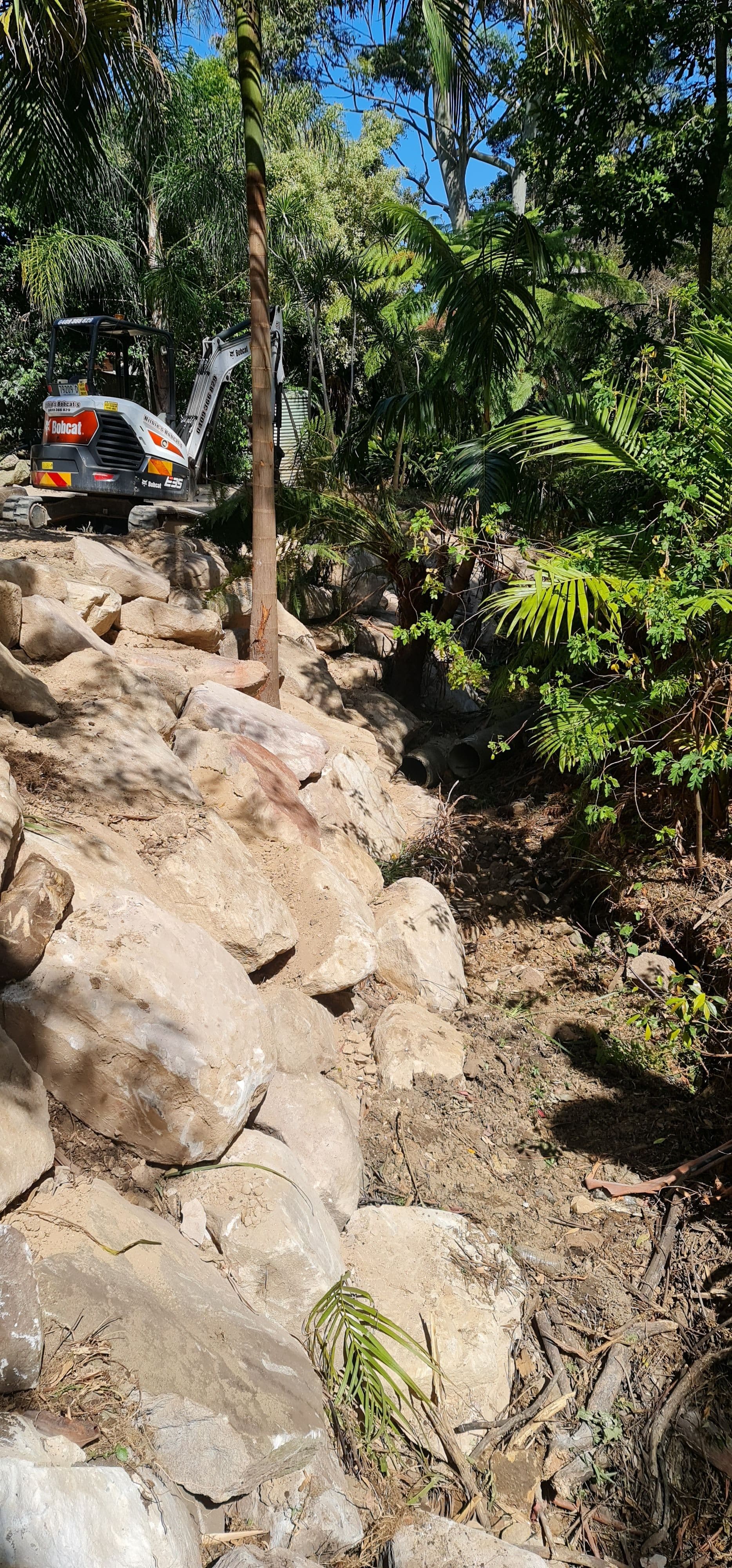 Excavator placing rocks for retaining walls of a creek wall in pennant hills